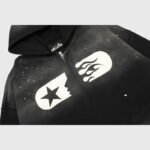 Close-up view of the Hellstar Studios black zip-up hoodie featuring a white graphic print and flame design details.