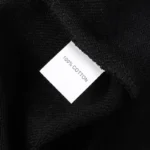 Close-up of the 100 percent cotton fabric tag inside a black Hellstar Studios zipper sweater for premium quality.