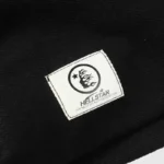 Close-up view of the official Hellstar Studios authentication tag on a black zipper sweater fabric surface.