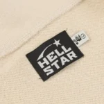 Close-up view of the Hellstar Studios Zipper Sweater brand tag featuring a black logo on beige fabric material.