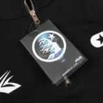 Close-up of the Hellstar Studios Zipper Sweater featuring a detailed graphic brand product label tag attached to zipper.