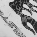 Close-up view of the Hellstar Thorn Glitter T-Shirt in white featuring a black flame logo with shimmer accents
