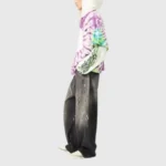 A side view of a model wearing a vibrant purple and green Hellstar tie-dye hoodie with unique streetwear graphics