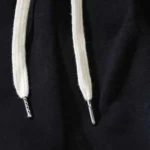 Close up of the cream white drawstring with metal aglets on the black fabric of Hellstar Uniform sweatpants.
