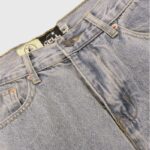 Close-up view of Hellstar premium vintage washed denim jeans featuring signature custom hardware and button closure.