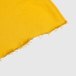 Close-up view of bright yellow fabric featuring a distressed raw hem with visible fraying threads on a white background.